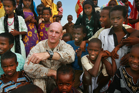 1st Place Photojournalism by Sgt. Alex Kleinsmith: Sgt. Matthew OBrian, a section leader and Nashville, Tenn., native with Battery A, 3rd Low Altitude Air Defense Battalion, watches a performance in Chebellier by the nine-piece U.S. Central Command Air Forces Band Live Round. Throughout the performance, OBrian helped the children learn the names of different instruments.